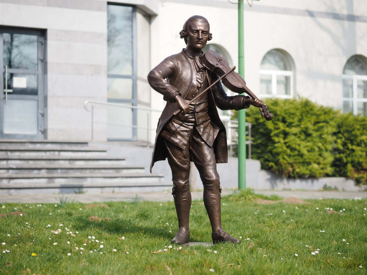 Lifesize bronze sculpture of Mozart playing the violin, showcasing fine detail and elegance in outdoor display.