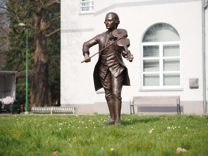 Lifesize bronze sculpture of Mozart playing the violin outdoors, showcasing detailed craftsmanship and brown patina.