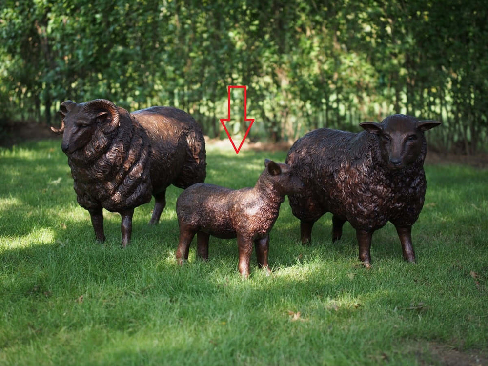 Lifesize bronze sculptures of a lamb, ram, and sheep in a grassy outdoor setting.
