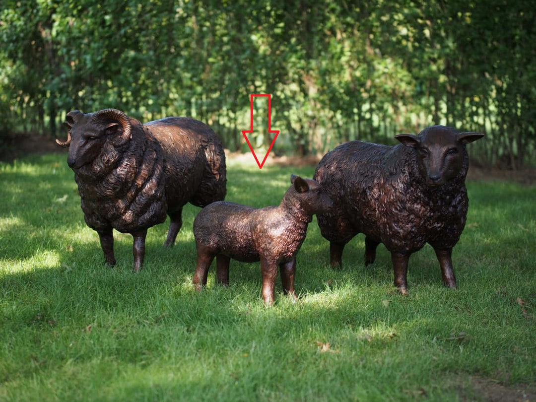 Lifesize bronze sculptures of a lamb, ram, and sheep in a grassy outdoor setting.