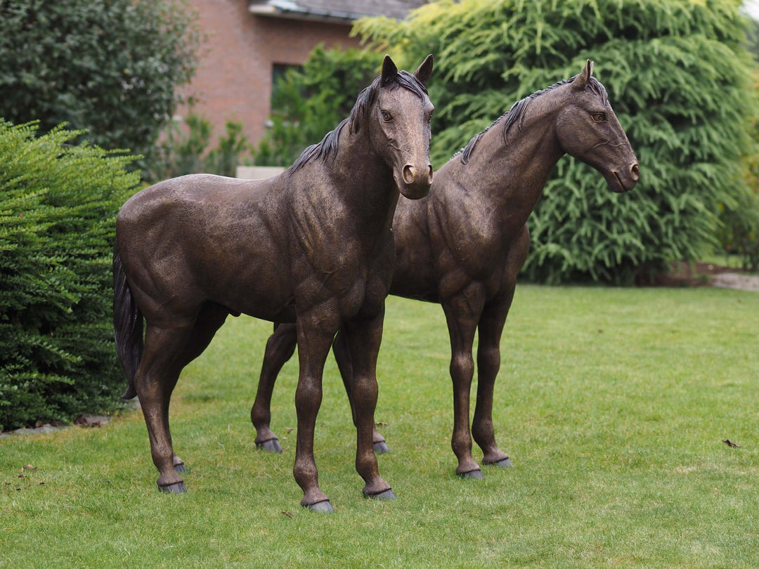 Pair of large bronze horse sculptures showcasing elegance and realism in a garden setting.