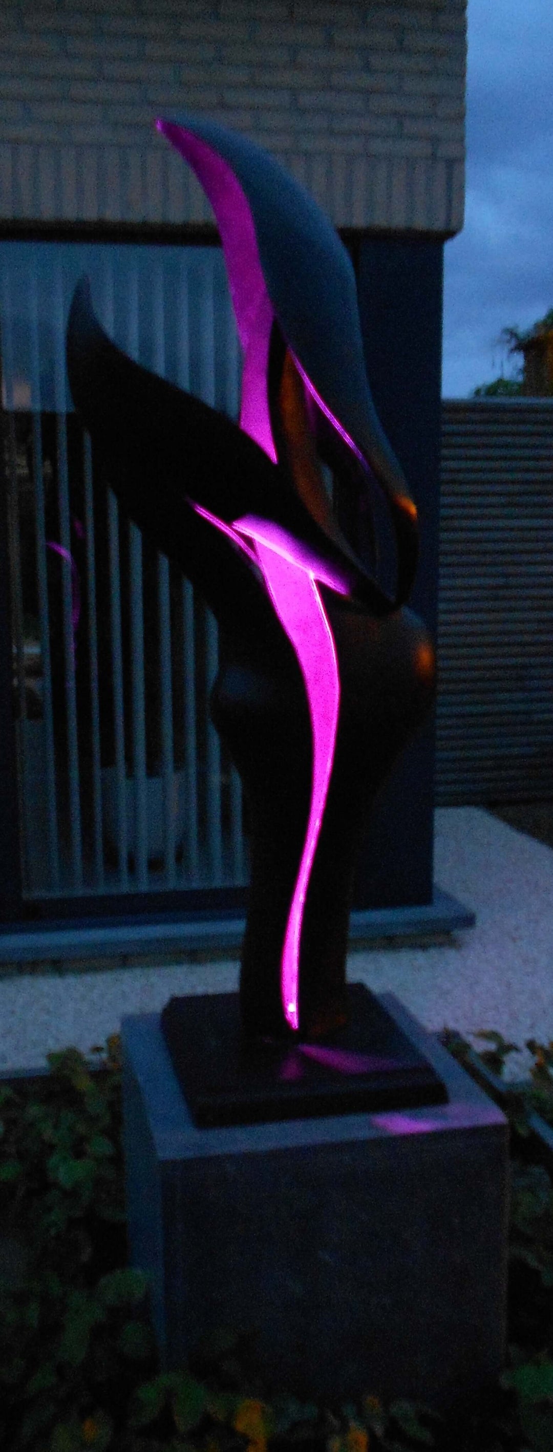 Modern illuminated sculpture featuring flowing forms in dark colors with purple lighting, perfect for outdoor settings.