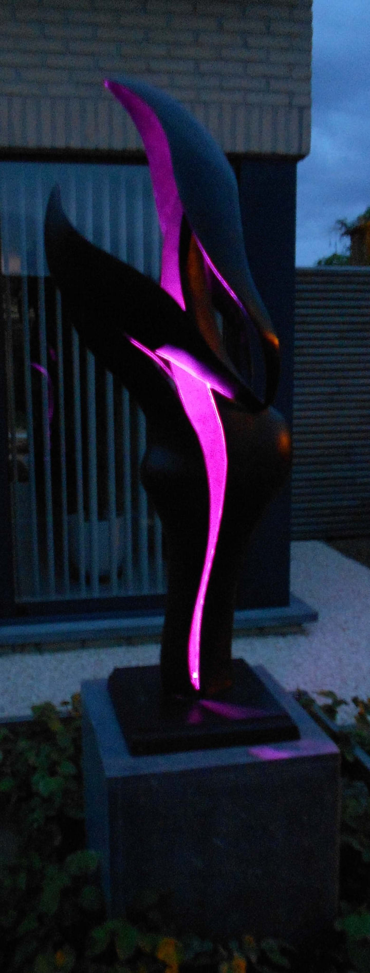 Modern illuminated sculpture featuring flowing forms in dark colors with purple lighting, perfect for outdoor settings.