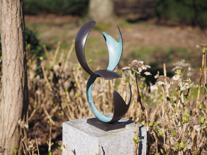 Modern bronze figure with abstract forms, showcasing harmony and unity, set in a garden with natural background.