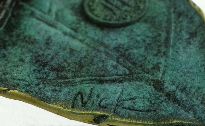Signature 'Nick' on a bronze sparrow sculpture, showcasing intricate patina and craftsmanship details.