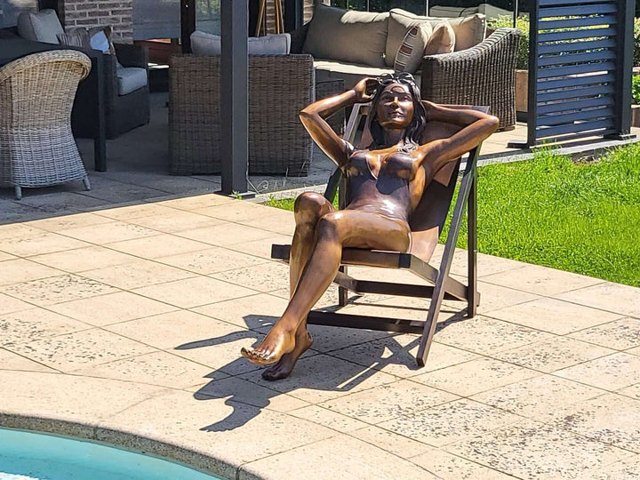 Large bronze sculpture of a sunbathing woman lounging by the pool on a sunny day, showcasing elegant design.