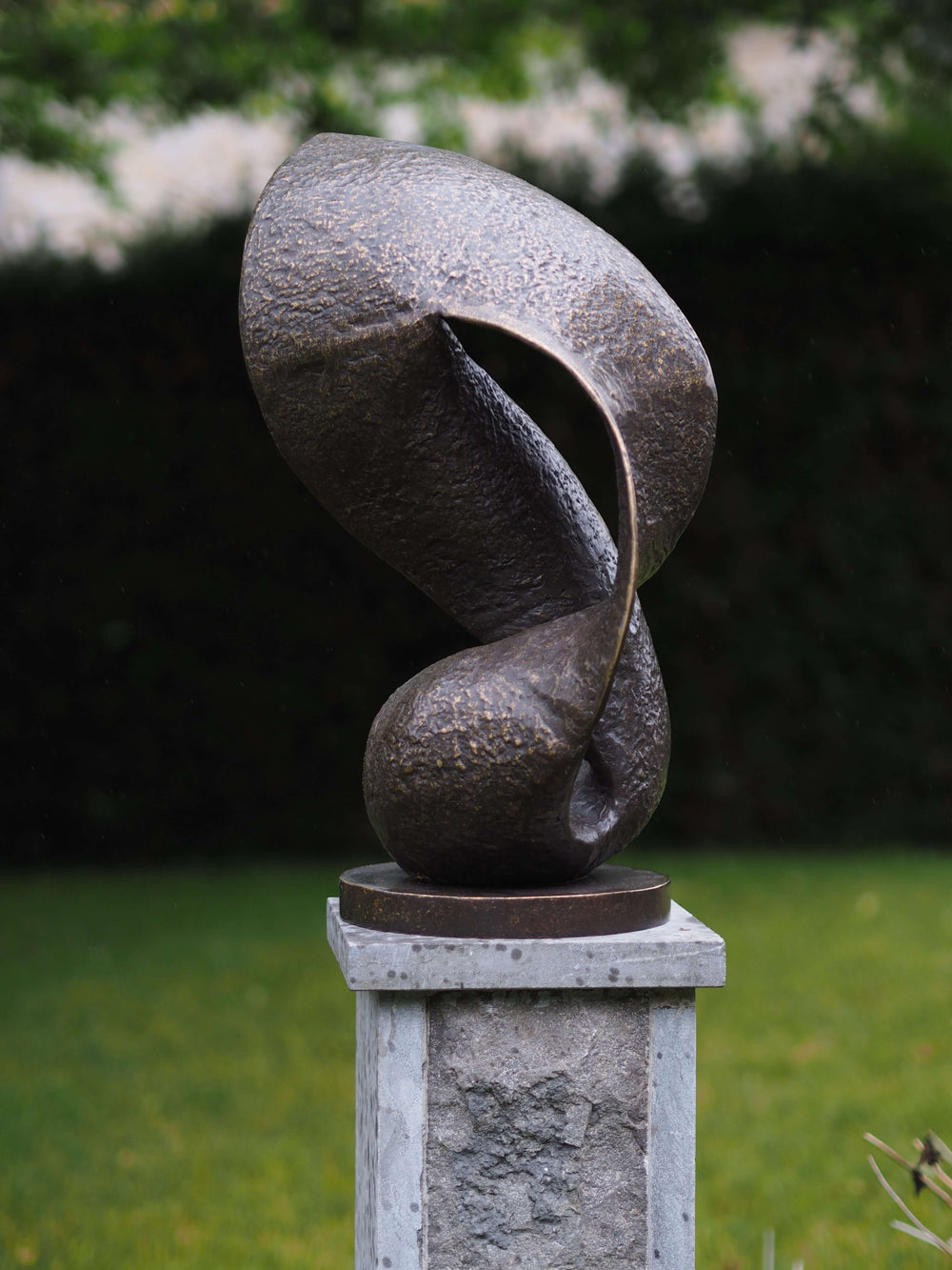 Modern bronze sculpture of a wave in motion on a stone pedestal, showcasing elegant fluid curves and textured finish.